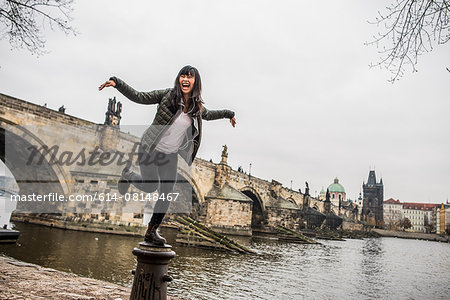 Woman balancing on bollard in front of Charles Bridge, Prague
