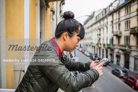 Side view of woman leaning against balcony using smartphone, Milan, Italy