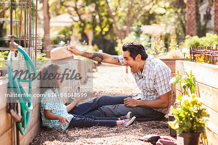Mid adult man  putting fedora on daughter in community garden