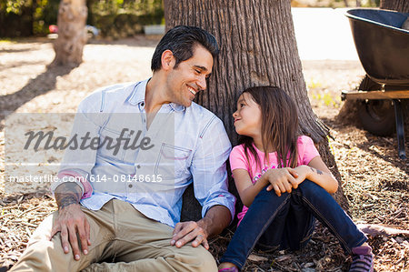 Girl and father leaning against tree in community garden