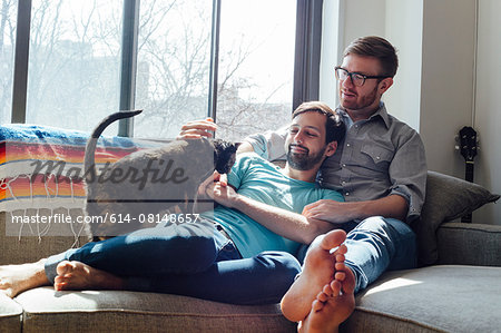 Male couple relaxing on sofa together with cat