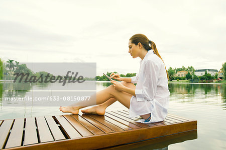 Woman relaxing on lake dock using digital tablet