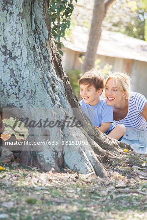 Young boy and mother hiding behind tree, playing hide-and-seek