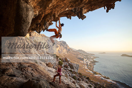 Young woman climbing on cliff, female partner belaying