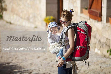Young woman tourist carrying her little son in sling