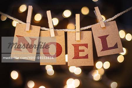 The word NOEL printed on clothespin clipped cards in front of defocused glowing lights.