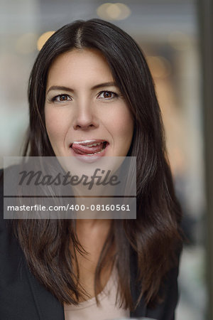 Attractive woman licking milky foam off her lips with a sensual gesture and smile as she sits in a cafeteria enjoying a cup of cappuccino, closeup head and shoulders