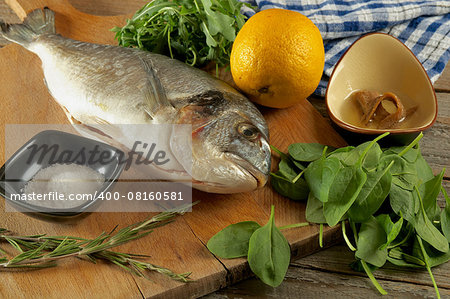 Cooking Raw Dorado Fish with Greens, Herbs, Spices, Anchovies and Lemon on Wooden Cutting Board closeup