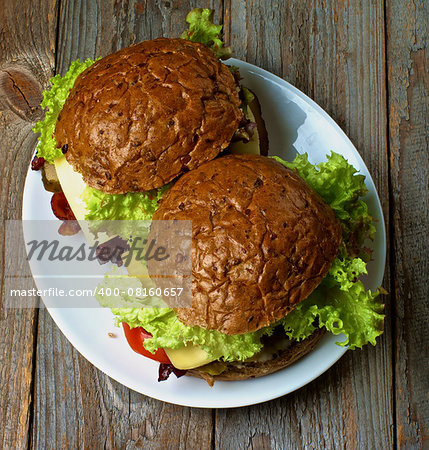 Homemade Hamburgers with Roasted Beef, Lettuce,Tomato, Onions, Cheese and Bacon with Whole Wheat Bun on White Plate on Rustic Wooden background. Top View