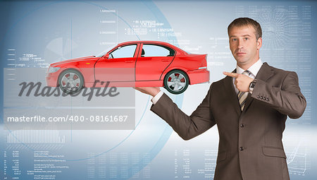 Businessman holding red car and looking at camera on abstract blue background