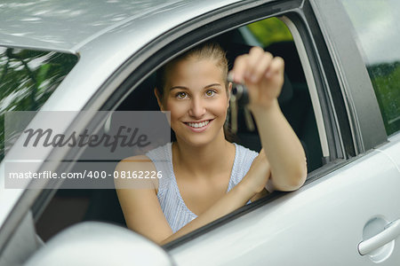 Young Pretty Woman Sitting Inside her Car, Smiling at the Camera While Showing Keys on her Hand.