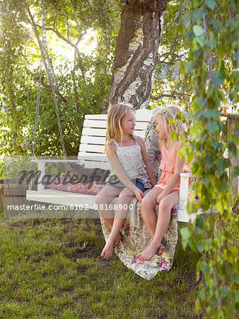 Girls on hanging bench in garden