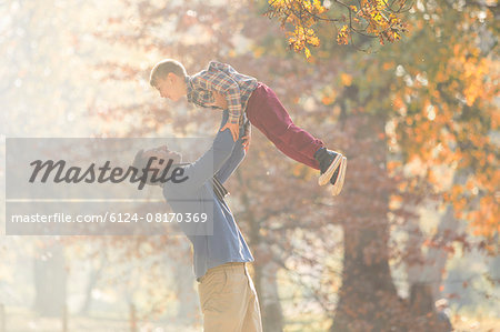 Father lifting son overhead in woods with autumn leaves