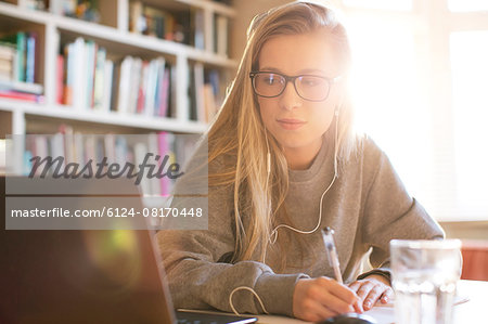 Teenage girl with headphones doing homework with laptop
