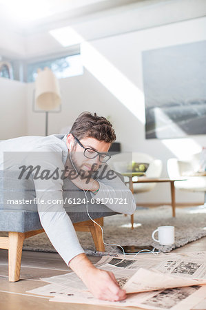 Man with headphones reading newspaper and drinking coffee in living room