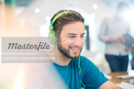 Smiling creative businessman listening to headphones in office