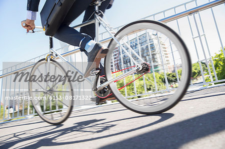 Low section businessman in suit riding bicycle on sunny urban sidewalk