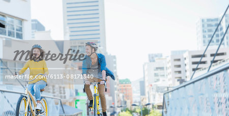 Friends with helmets riding bicycles over urban footbridge