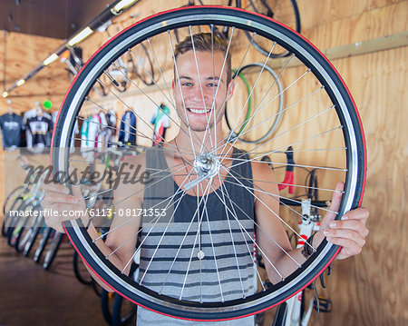 Portrait smiling young man holding bicycle wheel in bicycle shop