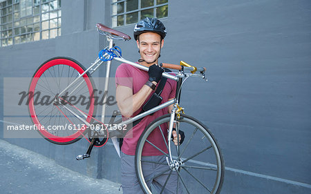 Portrait smiling young man carrying bicycle on urban sidewalk
