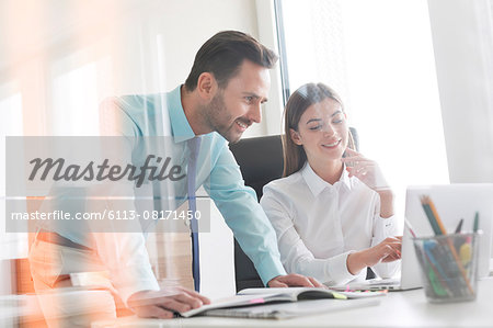 Businessman and businesswoman working at laptop in office