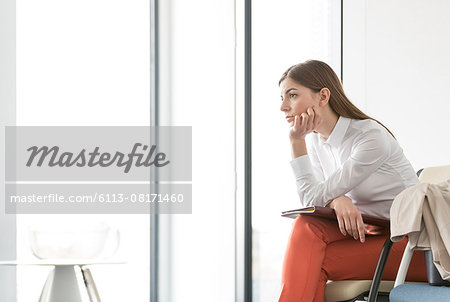 Pensive brunette businesswoman looking out office window with hand on chin