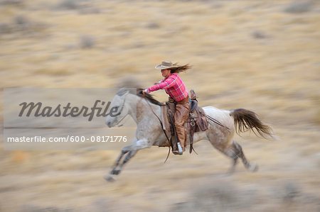 Blurred motion of cowgirl on horse galloping in wilderness, Rocky Mountains, Wyoming, USA