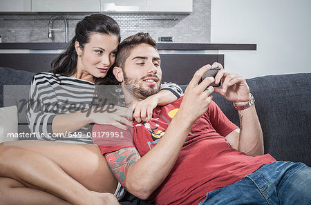 Young couple reclining on sofa taking smartphone selfie