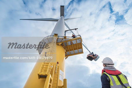 Engineers winch tools up wind turbine from boat at offshore windfarm, low angle view
