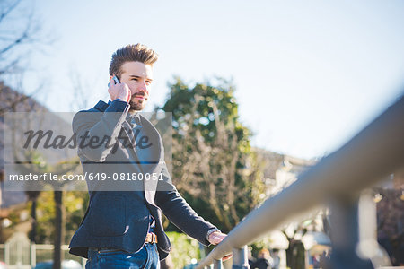Young man talking on smartphone whilst holding railing