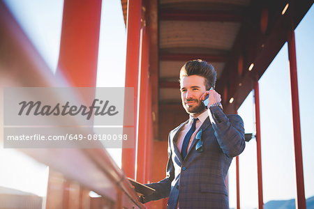 Young man with digital tablet chatting on smartphone on footbridge