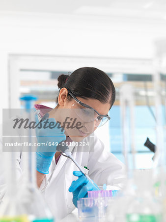 Young woman scientist pipetting sample into vial in a laboratory used for chemical and DNA testing Young woman scientist pipetting sample into vial in a laboratory used for chemical and DNA testing