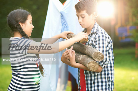Boy and sister preparing logs for campfire in garden