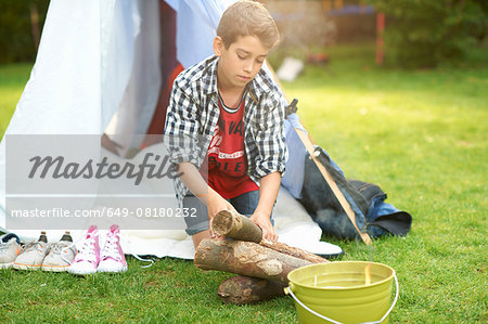 Boy preparing logs for campfire in garden