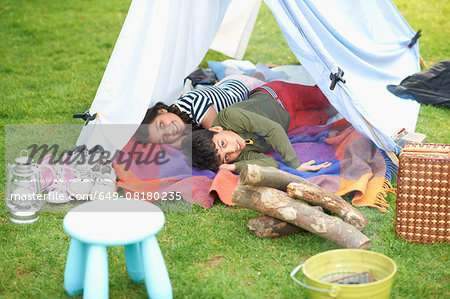 Brother and sister lying in homemade tent in garden