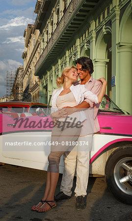 Young couple leaning against vintage convertible, Havana, Cuba