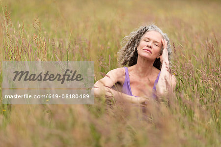 Mature woman sitting in long grass with eyes closed