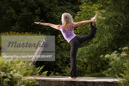 Mature woman practicing yoga dancer pose in garden