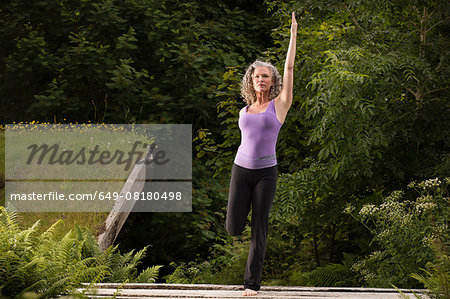 Mature woman practicing yoga pose on one leg in garden