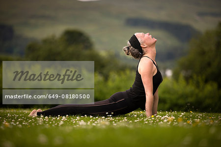 Mature woman practicing yoga upward dog in field