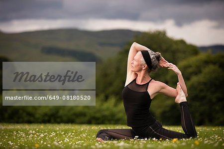 Mature woman doing splits practicing yoga in field