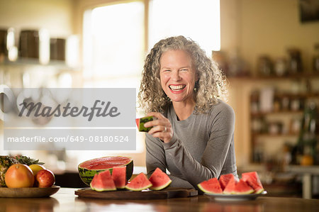 Portrait of mature woman eating watermelon in kitchen