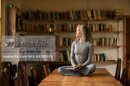 Mature woman sitting cross legged on kitchen table looking out of window