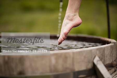 Bare foot of mature woman stepping into fresh cold water tub at eco retreat