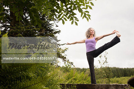 Mature woman practicing yoga pose on footbridge
