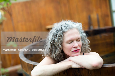 Mature woman resting on hands in hot tub at eco retreat