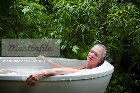 Mature woman relaxing in garden bubble bath at  eco retreat