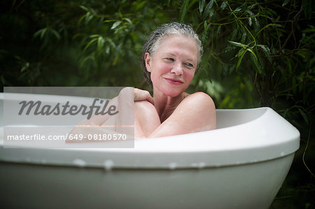 Mature woman hugging knees in garden bubble bath at  eco retreat