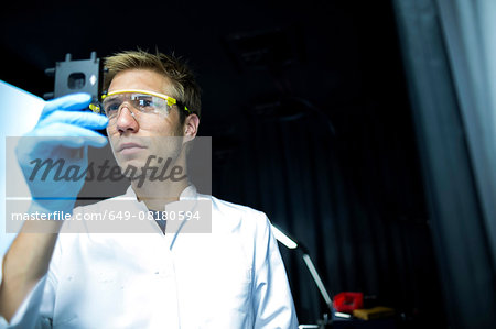 Male scientist holding up and scrutinizing specimen in lab cleanroom