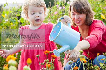 Mid adult mother and toddler daughter watering flower field